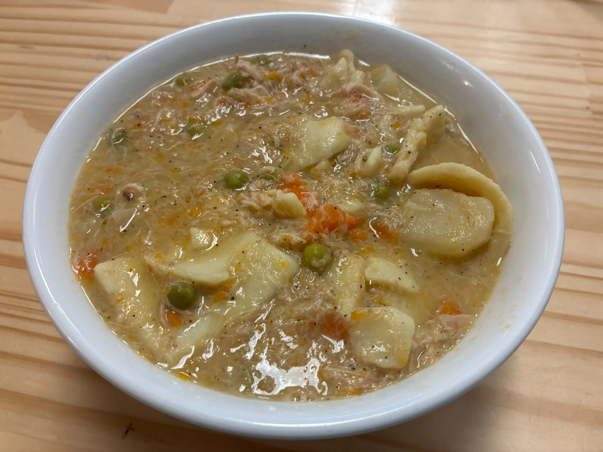 Creamy chicken pot pie soup with shredded chicken, peas, carrots, and homemade square dough noodles in a white bowl at Kat’s Café & Restaurant.