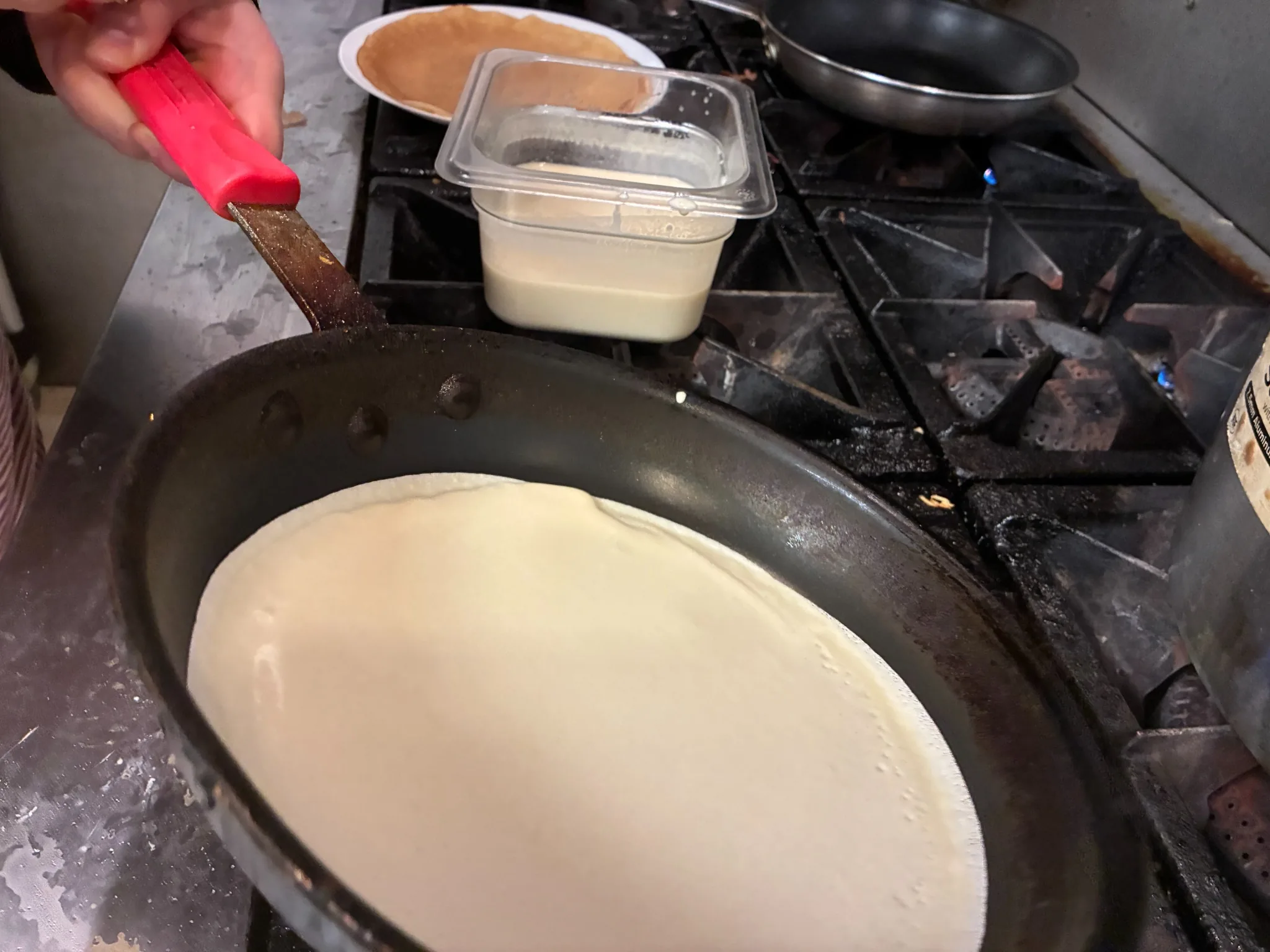 Crepe batter being spread into a thin layer in a hot pan in the kitchen at Kat’s Café & Restaurant.