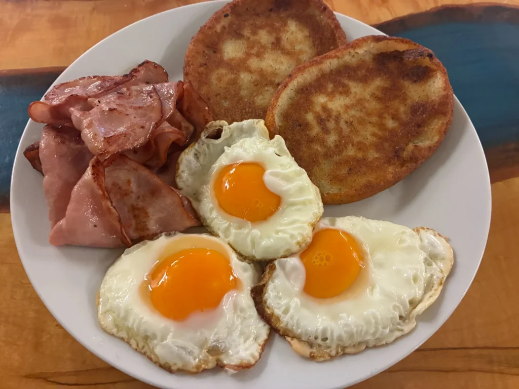 Three sunny-side-up eggs with grilled ham and two potato pancake blinis on a white plate at Kat’s Café & Restaurant.