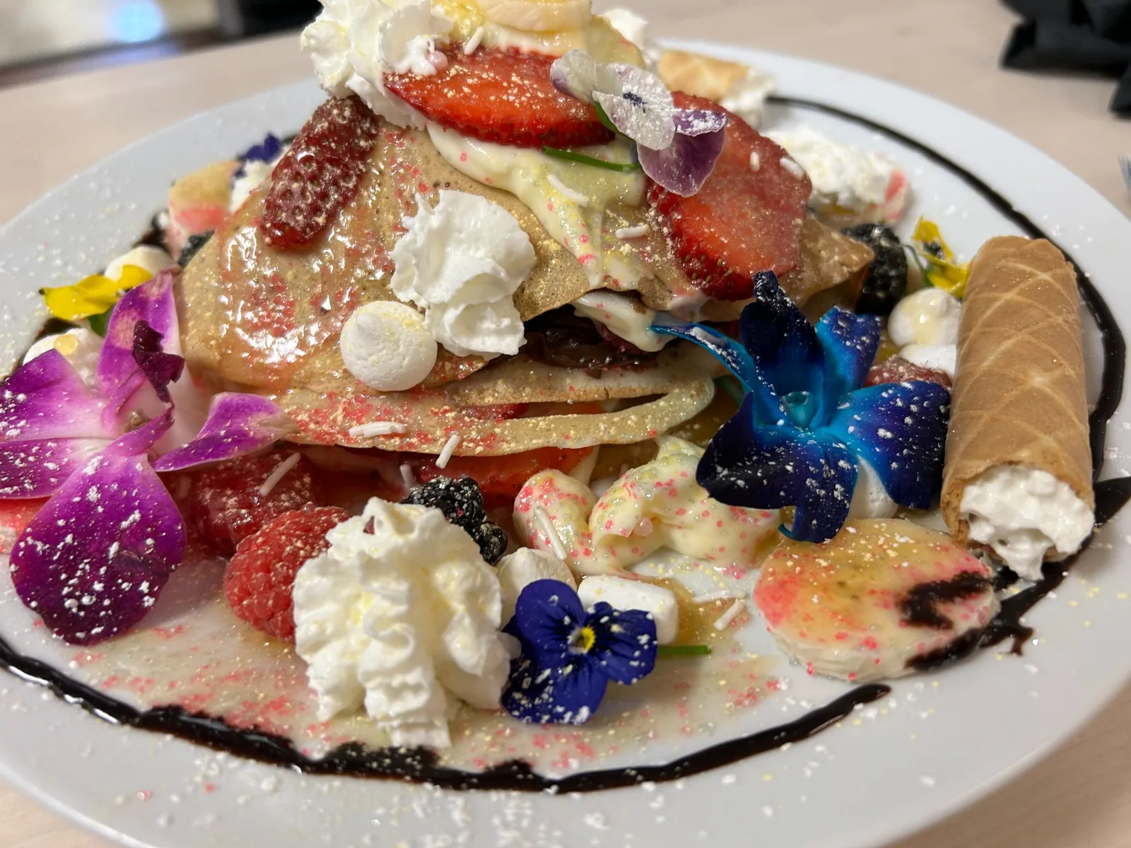 Everything crepe piled with strawberries, banana, berries, whipped cream, marshmallows, chocolate drizzle, edible flowers, and a cream-filled wafer roll served on a white plate at Kat’s Café & Restaurant.