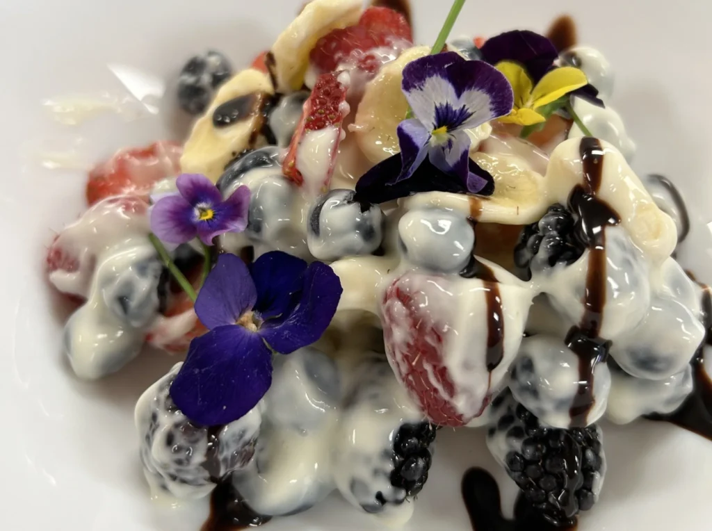 Fruit crème salad with berries and banana slices, topped with creamy dressing, chocolate drizzle, and edible flowers at Kat’s Café & Restaurant.