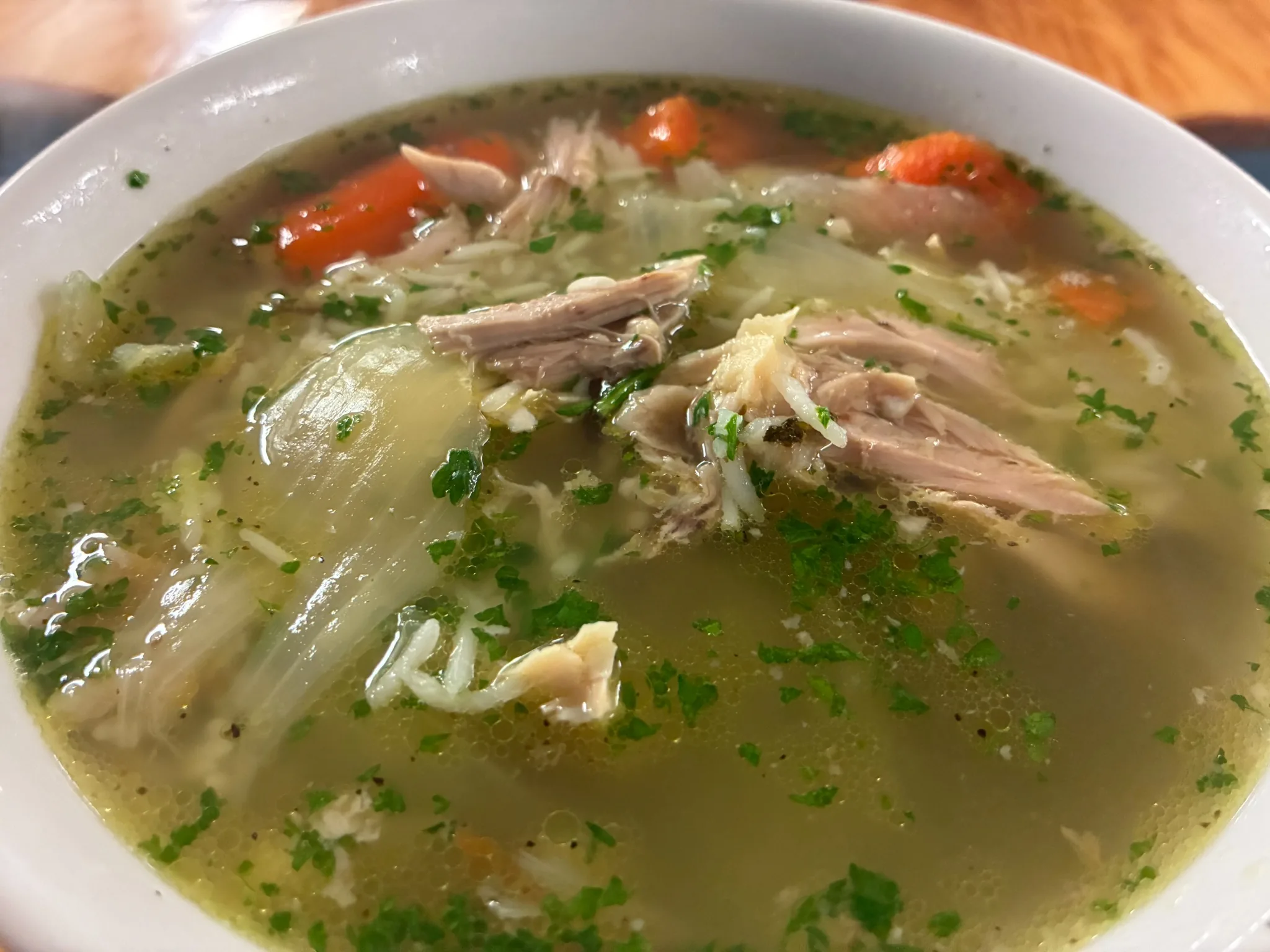 Clear chicken soup with tender chicken, carrots, rice, and fresh herbs in a white bowl at Kat’s Café & Restaurant.