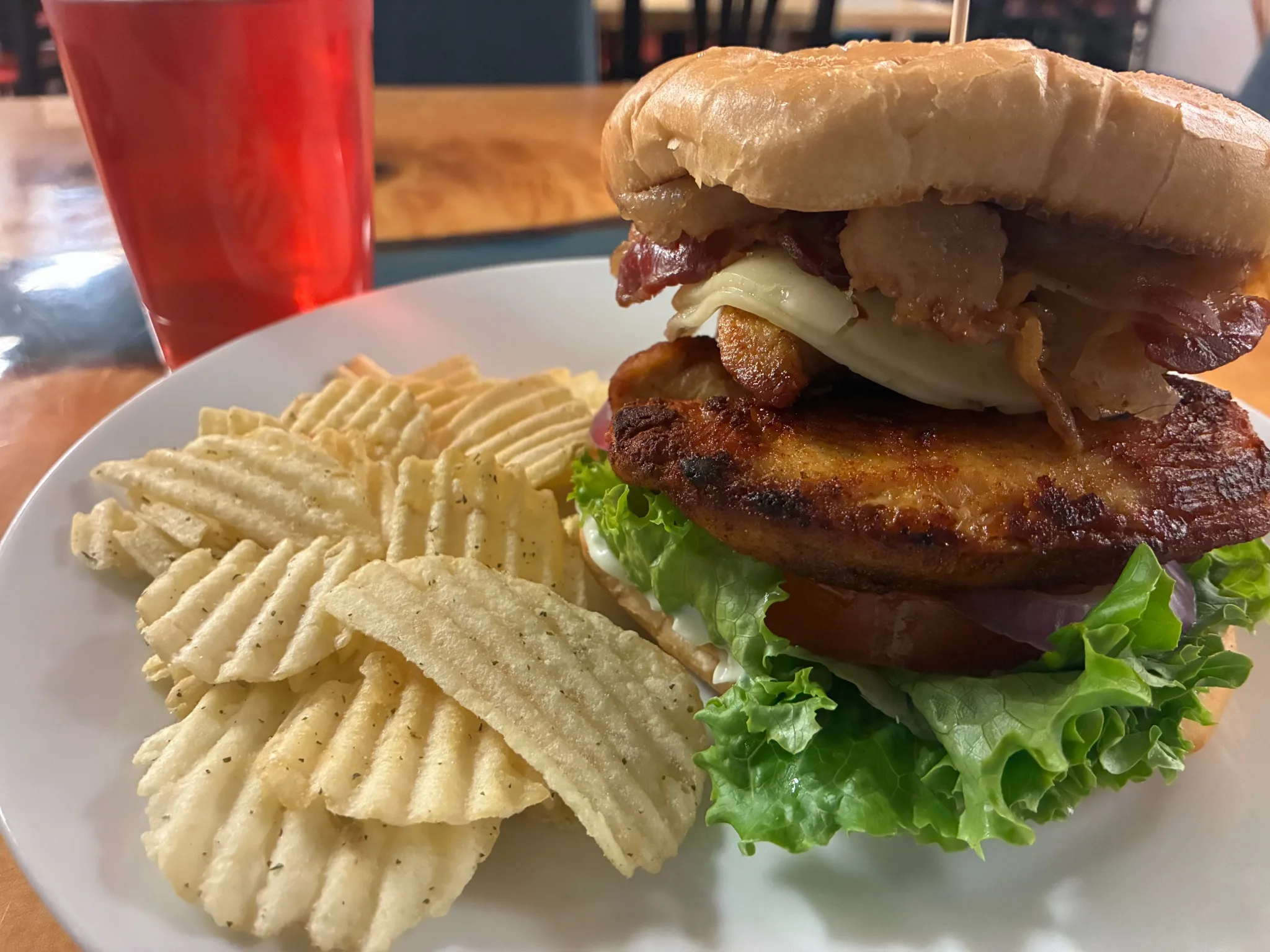 Grilled chicken and bacon sandwich with cheese, lettuce, tomato, and red onion, served with potato chips at Kat’s Café & Restaurant.