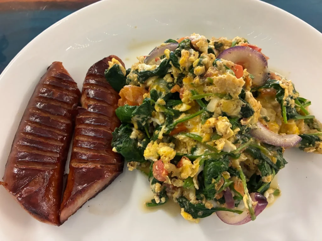 Grilled kielbasa beside scrambled eggs with spinach, red onion, and tomato served at Kat’s Café & Restaurant.