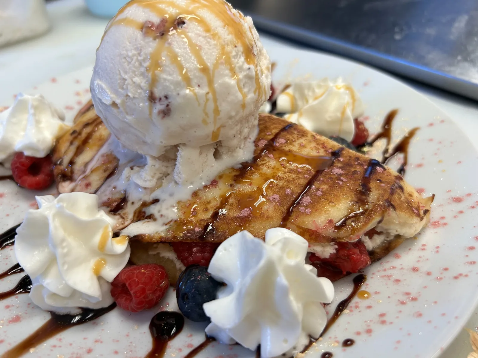 Fruit-filled, sweet cheese dessert crepe topped with a scoop of ice cream and served with raspberries, blueberries, whipped cream, chocolate, and caramel drizzle at Kat’s Café & Restaurant.