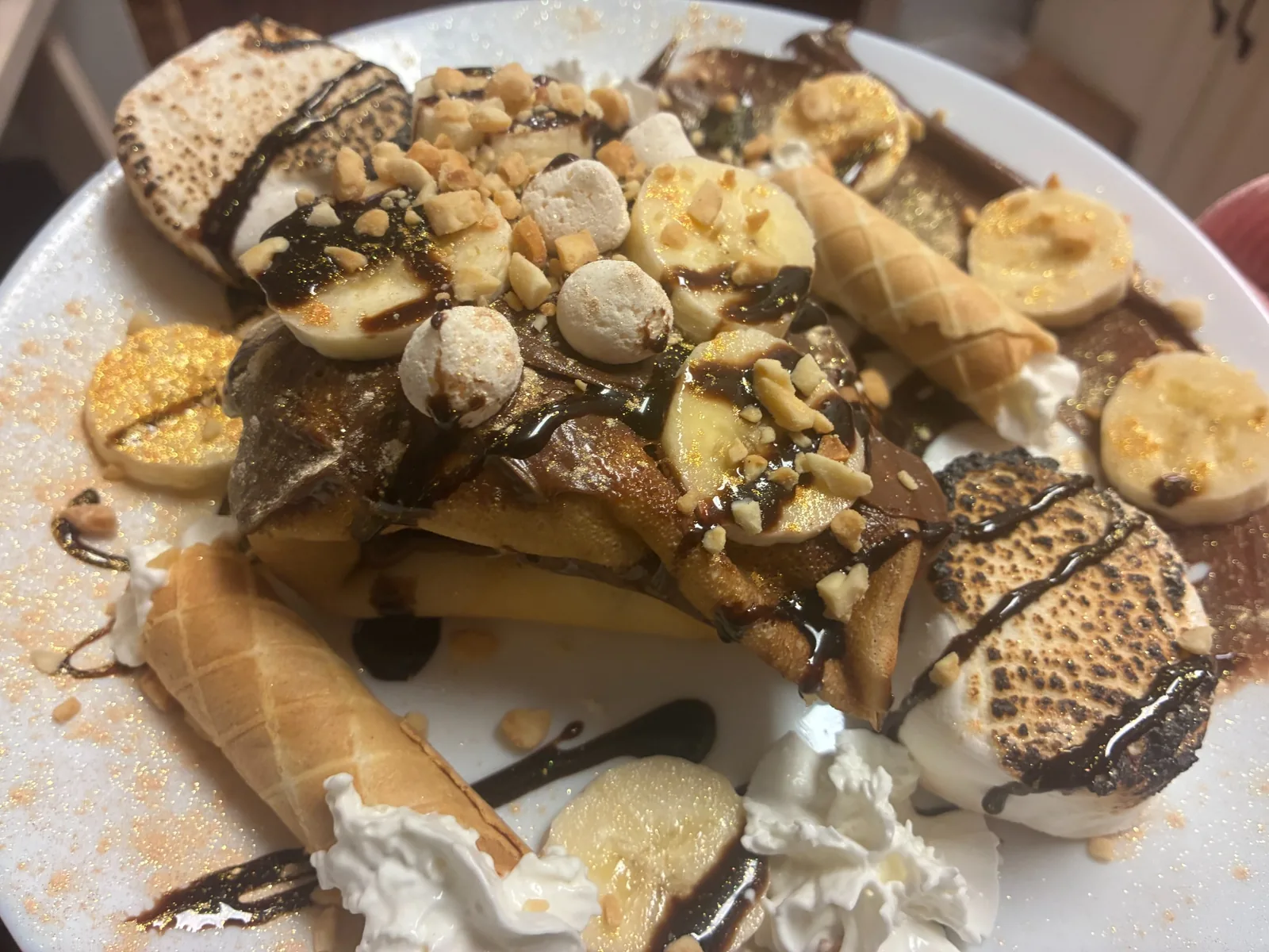 Nutella hazelnut crepe topped with banana slices, toasted marshmallows, chopped nuts, whipped cream, and chocolate drizzle on a white plate at Kat’s Café & Restaurant.