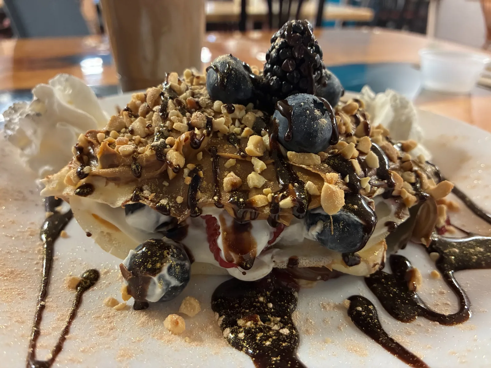 Close-up of a Nutella crepe layered with whipped cream, blueberries, blackberries, and chopped nuts, finished with chocolate drizzle on a white plate served at Kat’s Café & Restaurant.