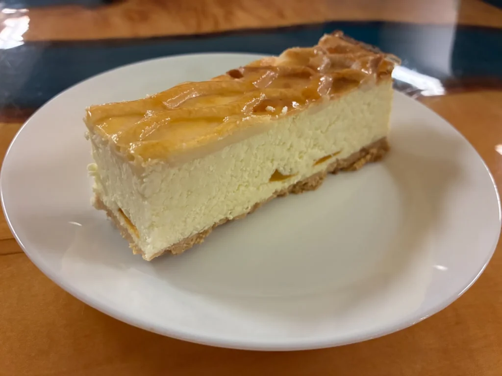 Peach cheesecake slice with glazed peach topping on a white plate at Kat’s Café & Restaurant.