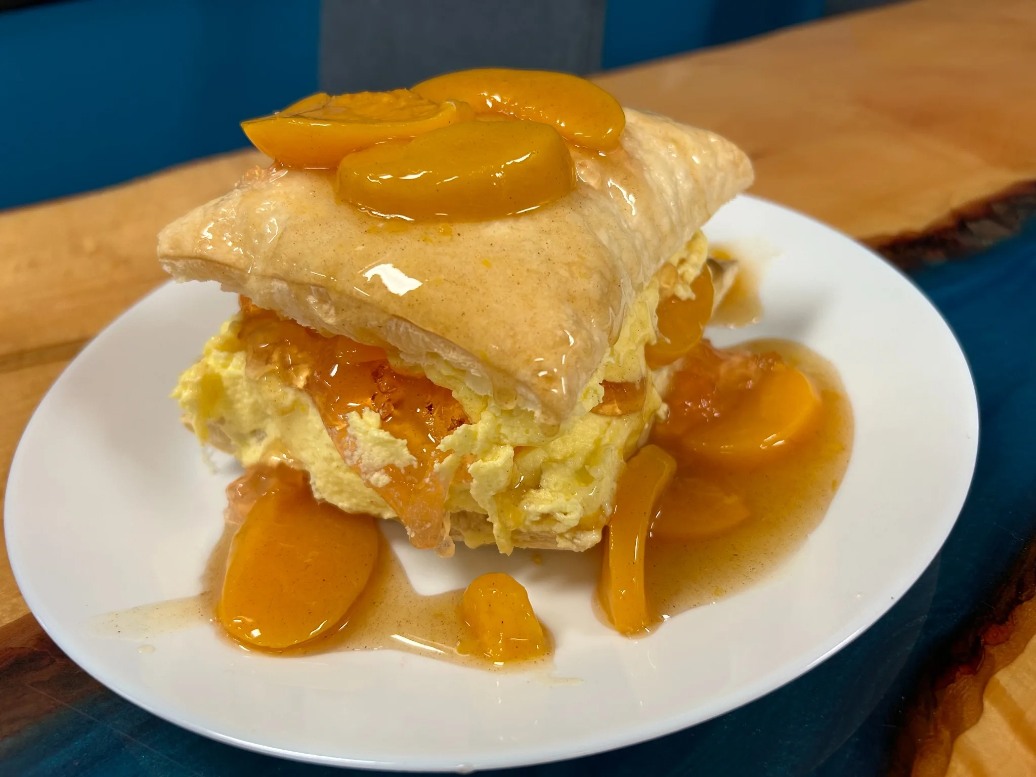 Dessert pastry filled with thick cream and topped with peaches and syrup on a white plate at Kat’s Café & Restaurant.