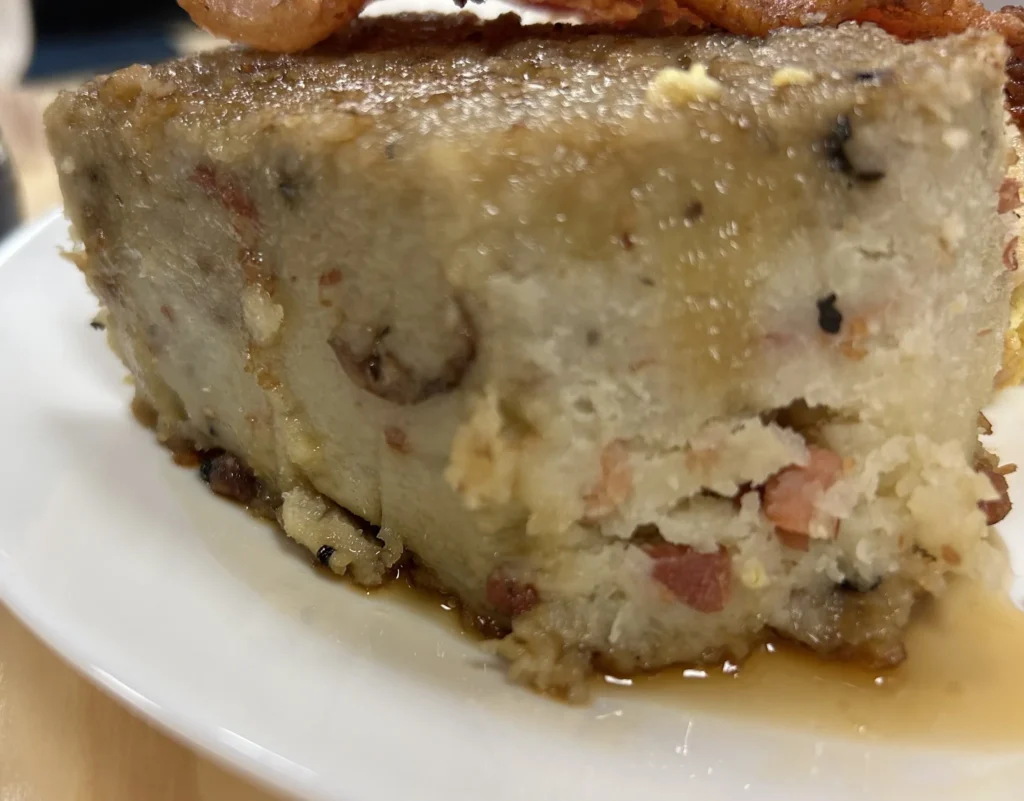 Close-up of a savory slice of potato babka with smoky meat pieces and maple syrup on a white plate at Kat’s Café & Restaurant.