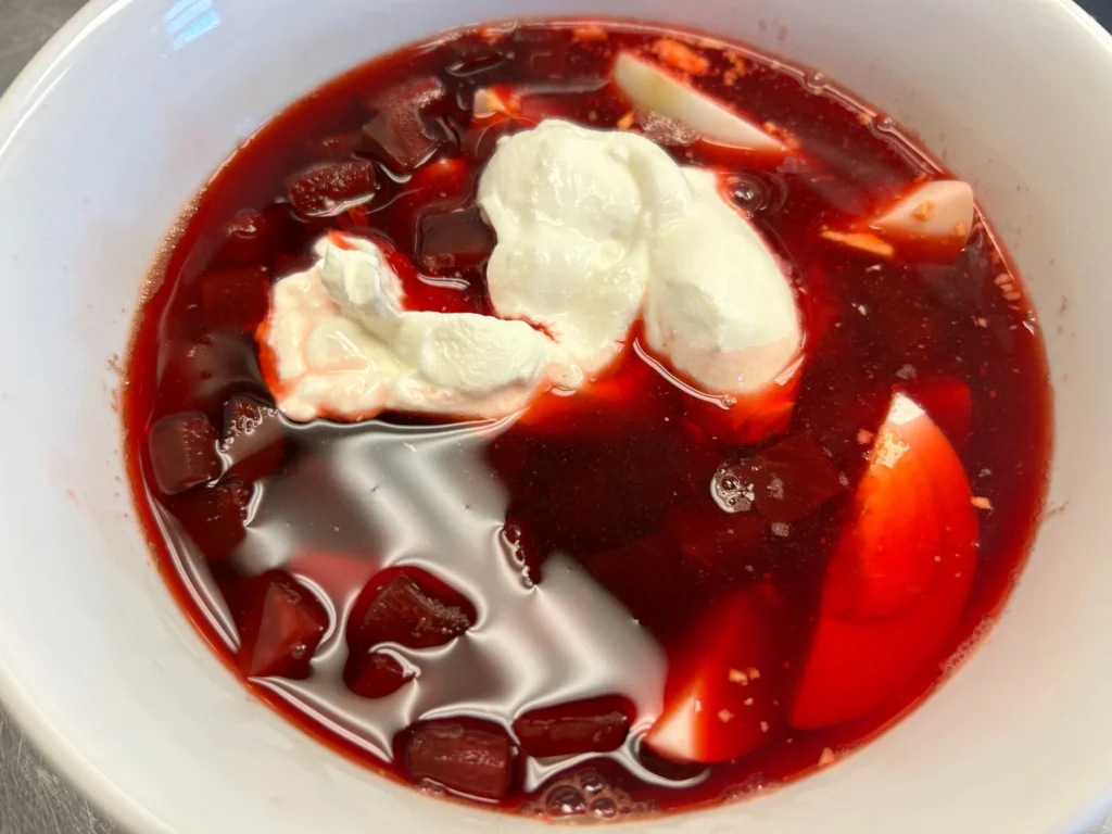 Bright red beet borscht with beet pieces, hard-boiled egg, and sour cream in a white bowl at Kat’s Café & Restaurant.