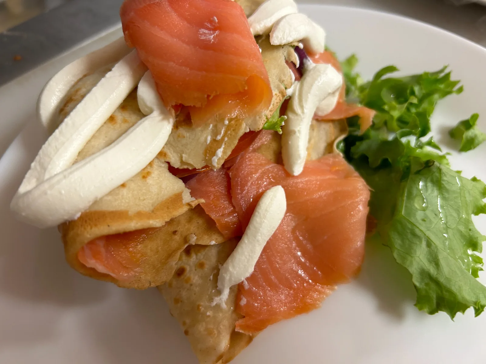 Folded salmon lox crepe layered with smoked salmon and cream cheese, served with red onion, tomatoes, and fresh greens at Kat’s Café & Restaurant.