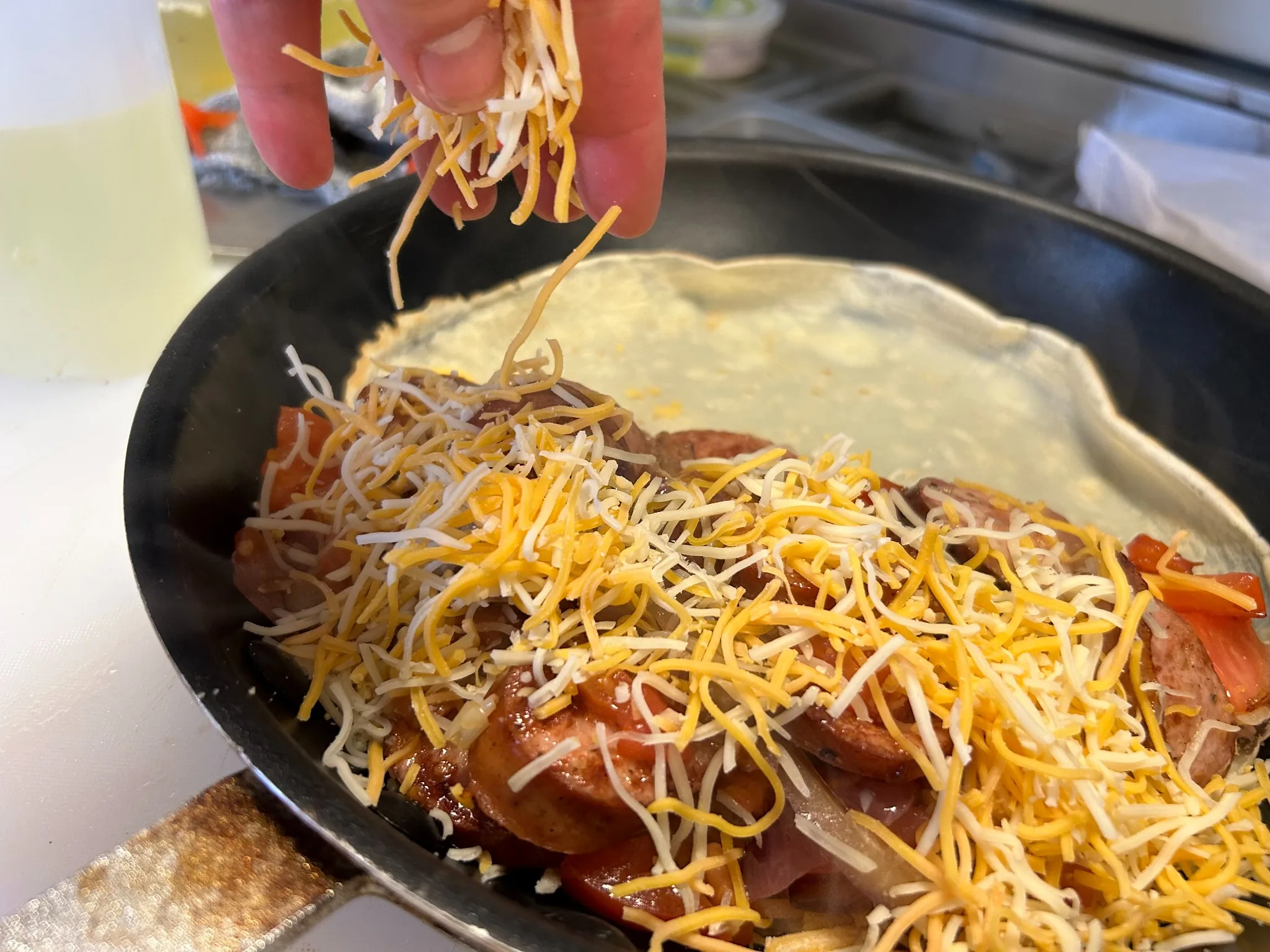 Shredded cheese being added to a savory kielbasa crepe in a skillet at Kat’s Café & Restaurant.