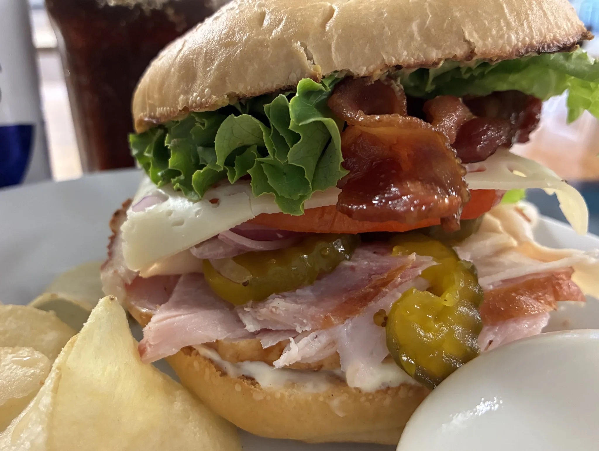 Stacked ham and bacon sandwich with cheese, pickles, tomato, red onion, and lettuce on a toasted roll at Kat’s Café & Restaurant.