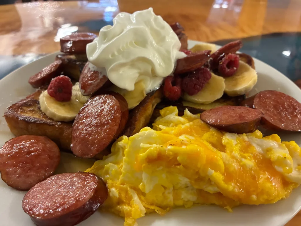 French toast topped with banana, raspberries, and whipped cream, served with scrambled eggs and sliced kielbasa at Kat’s Café & Restaurant.