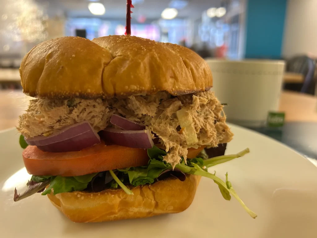Tuna salad sandwich with lettuce, tomato, red onion, and mixed greens on a roll at Kat’s Café & Restaurant.