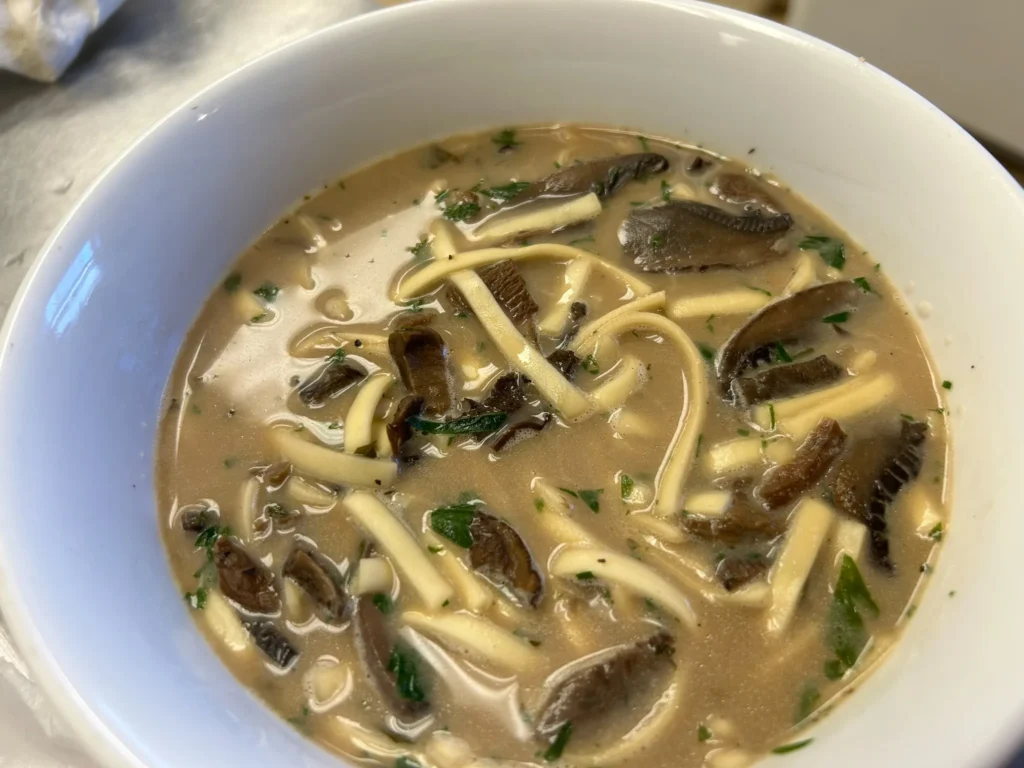 Vegetarian wild mushroom soup with sliced mushrooms, noodles, and fresh herbs in a white bowl at Kat’s Café & Restaurant.