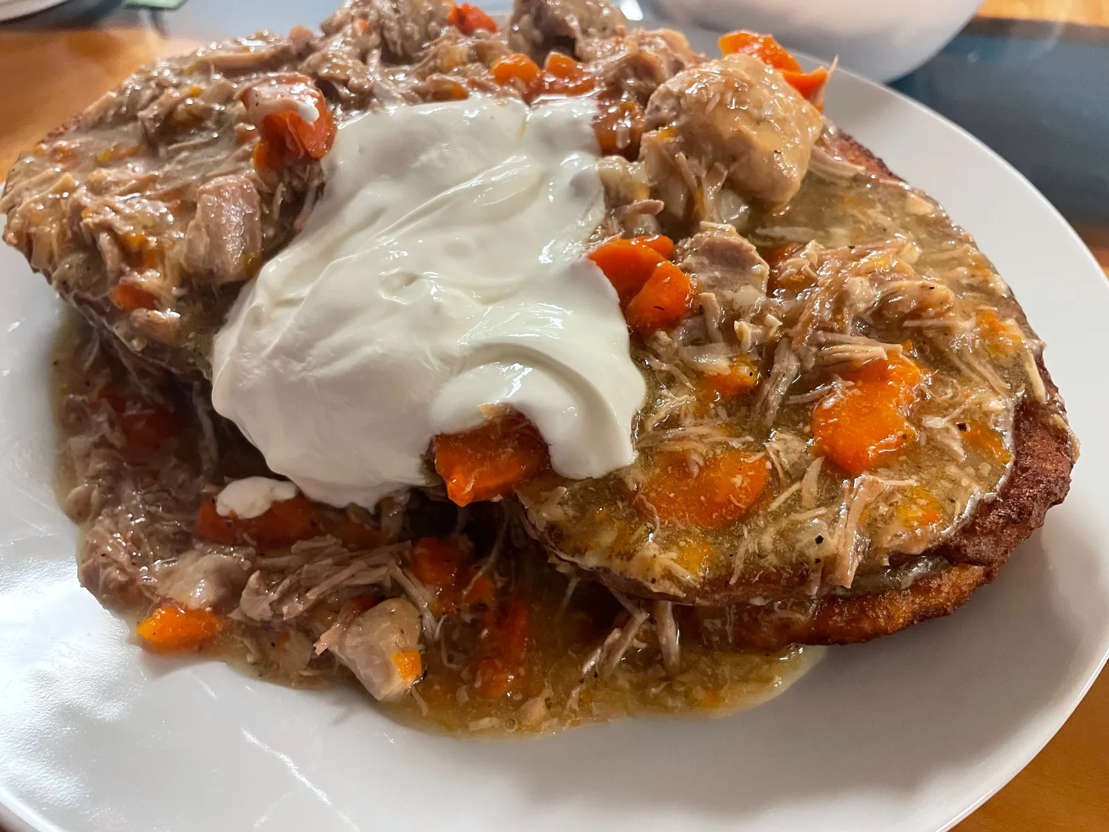 Large potato bleenie topped with pork goulash stew, carrots, meat gravy juices, and sour cream on a white plate at Kat’s Café & Restaurant.