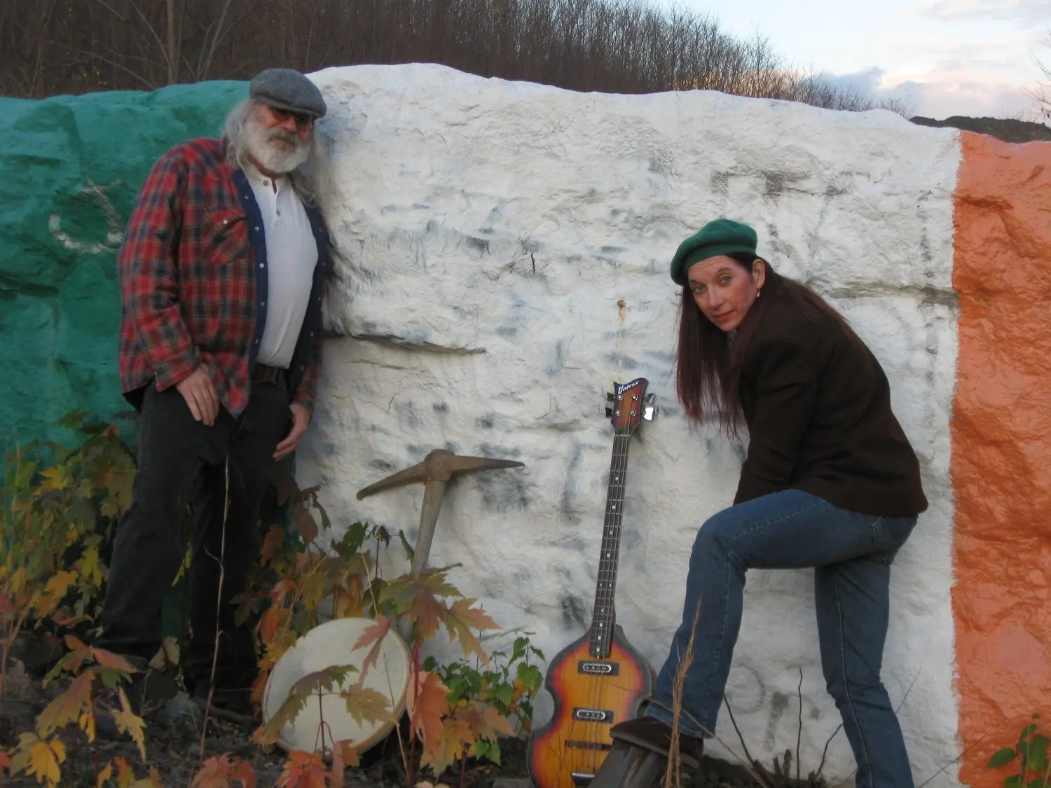 Two local musicians posing with a bass guitar and mining pick beside a large rock painted in the colors of the Irish flag in Schuylkill County, Pennsylvania, near Pottsville.