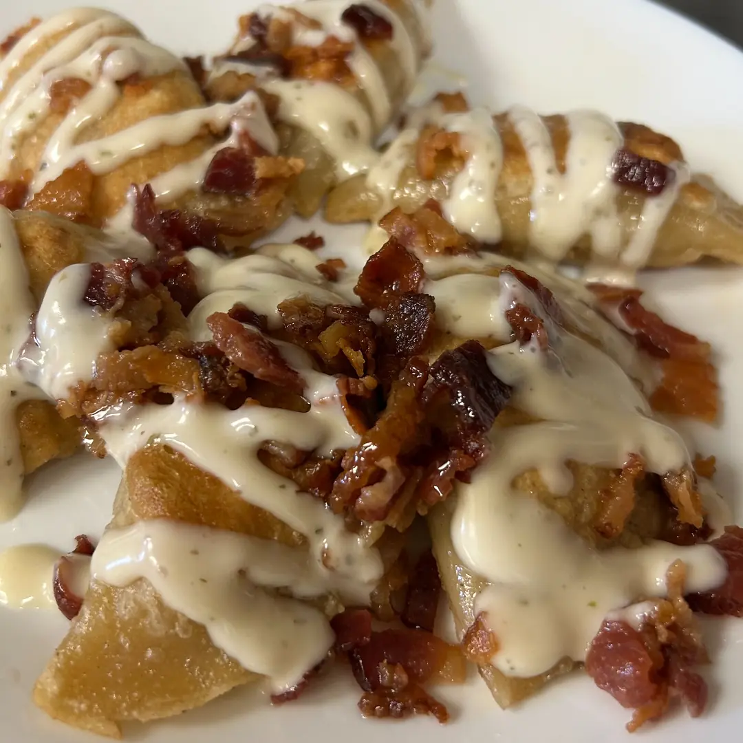 Six large handmade Polish pierogies at Kat’s Café & Restaurant made with scratch-made dough and our house-made seasoned chicken filling, pan-fried until crisp and finished with creamy ranch and real crumbled bacon.