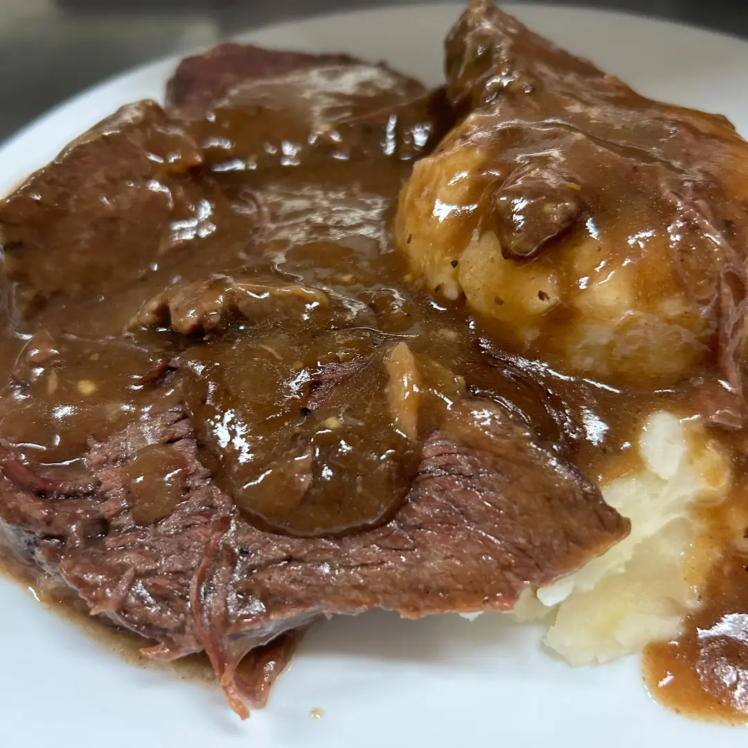 Tender slices of beef pot roast at Kat’s Café & Restaurant with mashed potatoes, covered in rich brown gravy on a white plate.