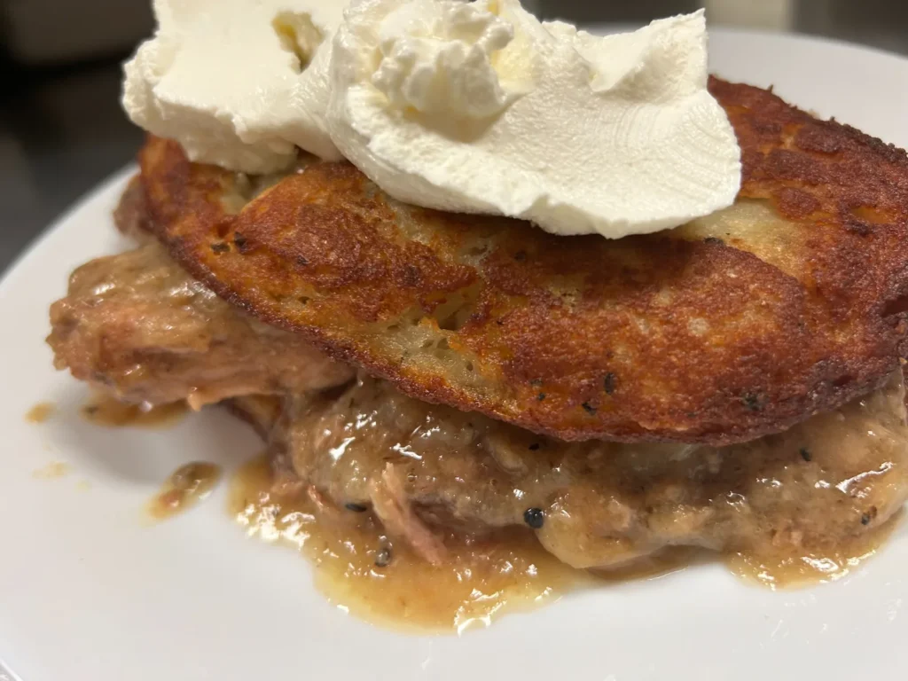 Golden-brown potato bleenie at Kat’s Café & Restaurant, layered over braised pork and gravy, topped with sour cream.
