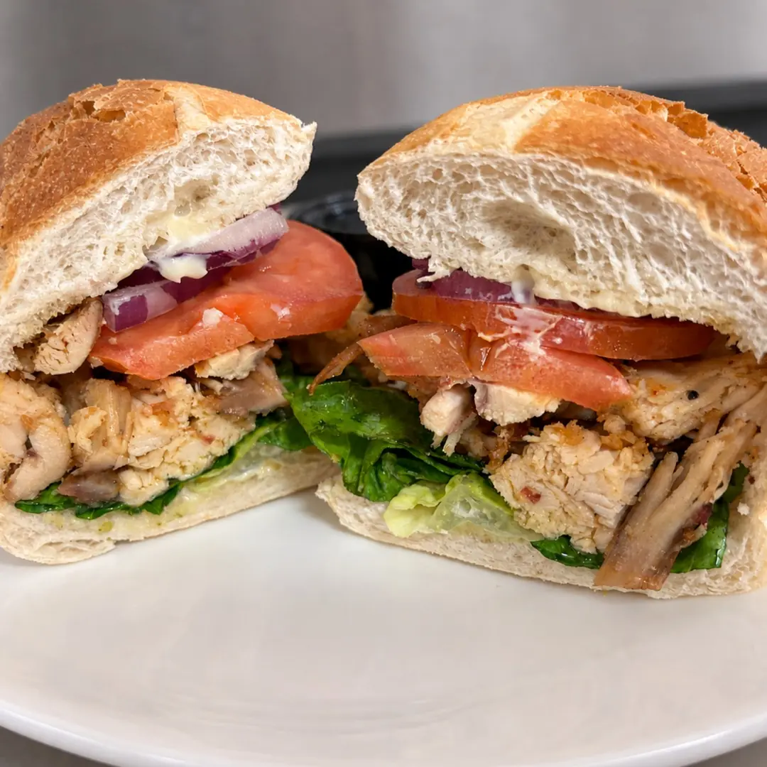 Grilled chicken sub at Kat’s Café & Restaurant with lettuce, tomato, red onion, and mayonnaise, served in two halves on a white plate.