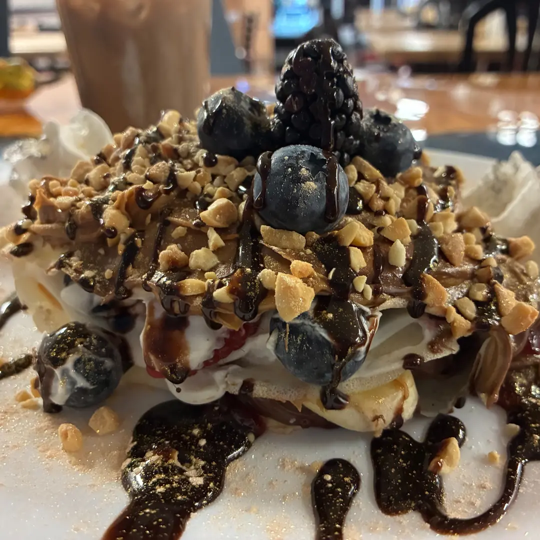 Kat's Everything Crepe layered with homemade sweet cream, Nutella, and assorted fresh fruit, topped with chopped peanuts, chocolate drizzle, and whipped cream.