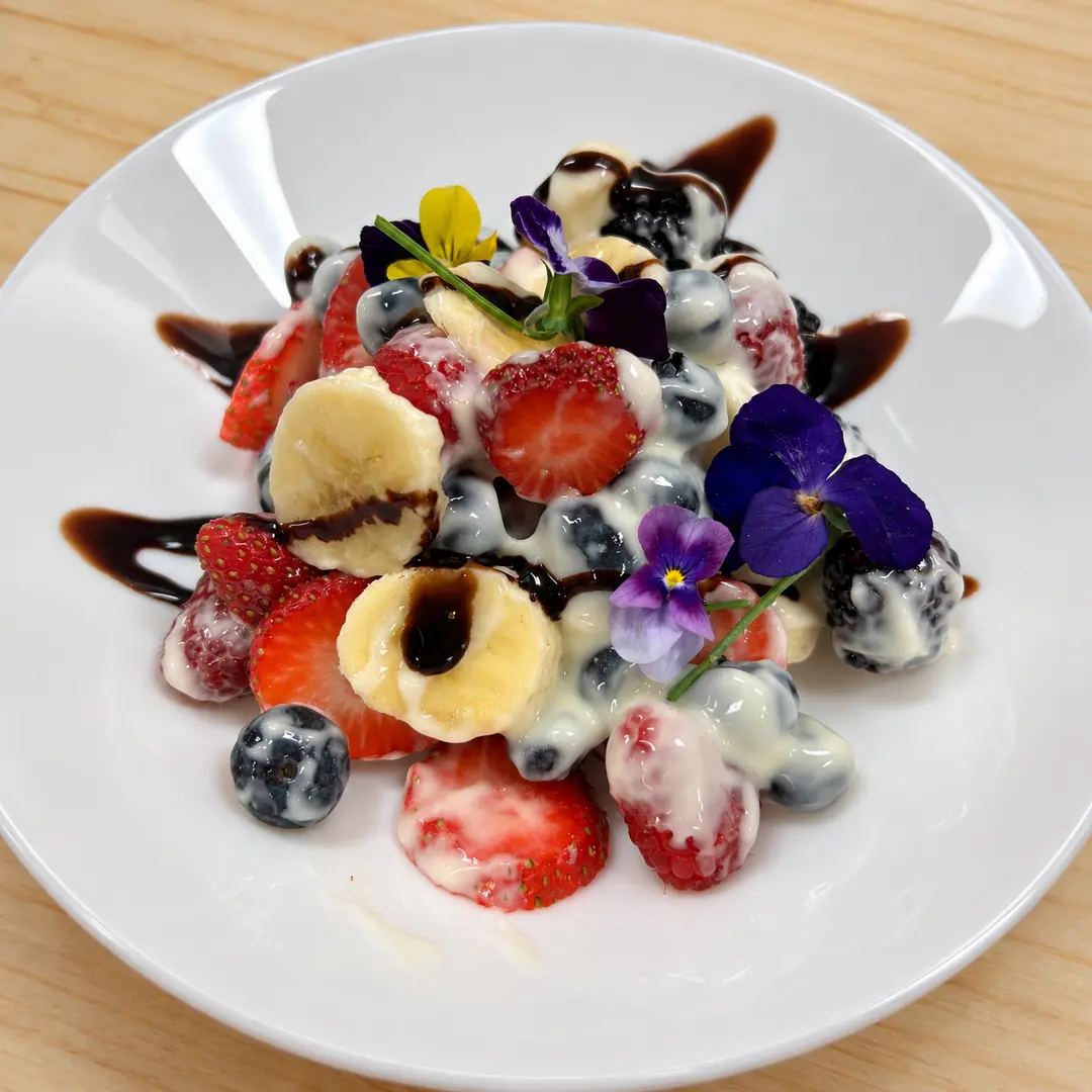 Fruits ’n Creme Salad at Kat’s Café & Restaurant with fresh berries, bananas, house-made sweet cream, chocolate drizzle, and edible flowers.