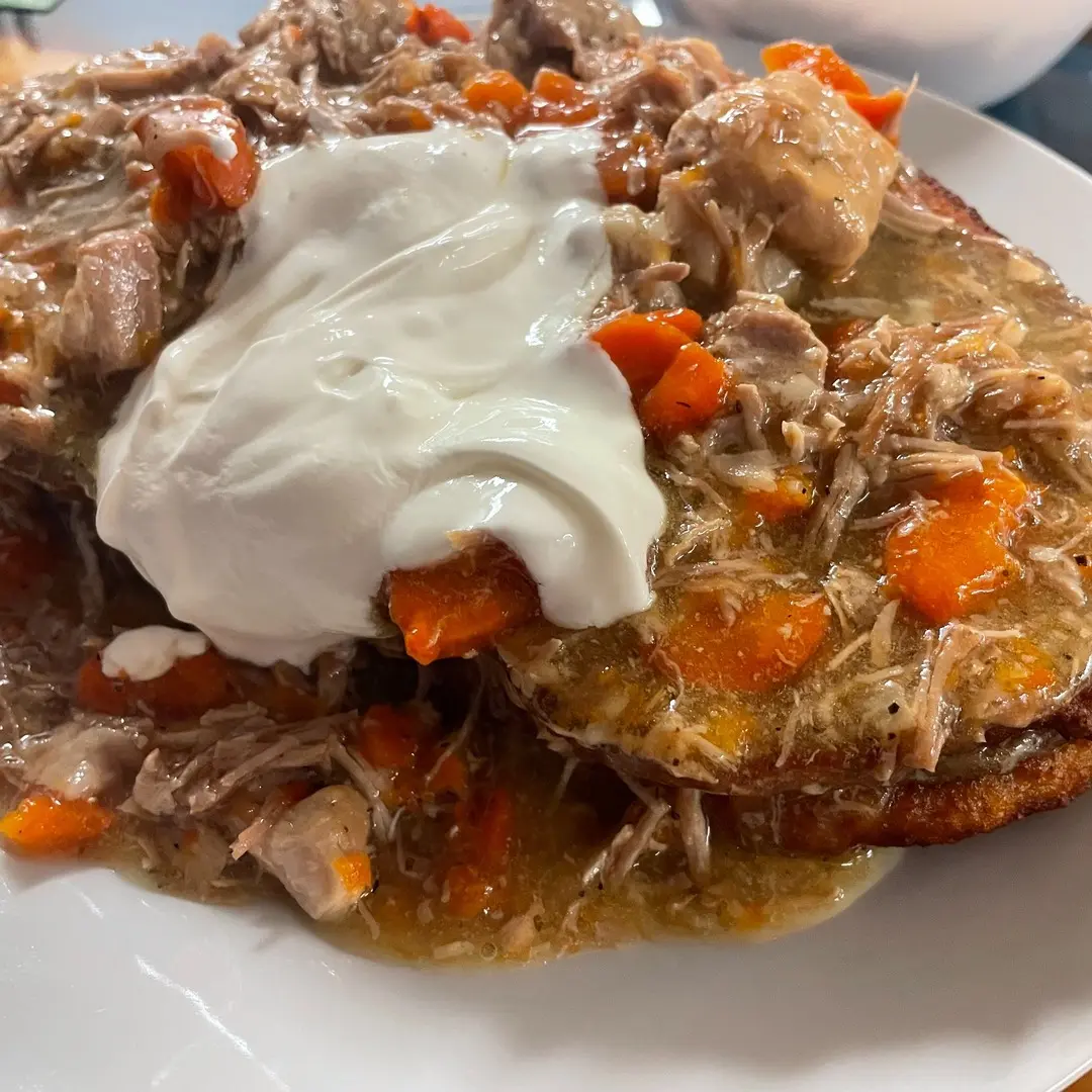 Golden potato bleenie topped with hearty goulash at Kat’s Café & Restaurant, having tender carrots, and sour cream, served on on a white plate.
