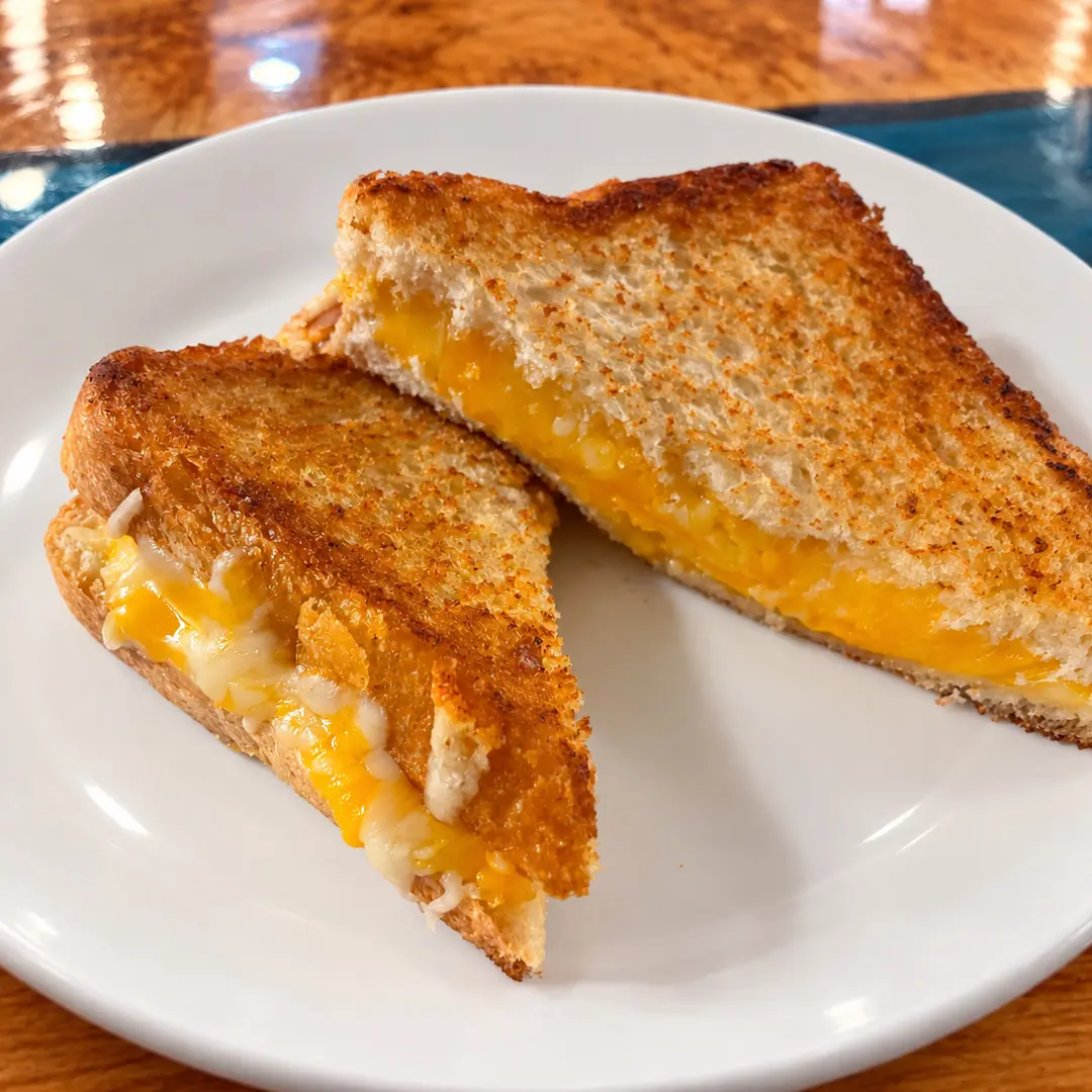 Golden-brown grilled cheese sandwich at Kat’s Café & Restaurant with melted cheese, cut into two triangular halves and served on a white plate.