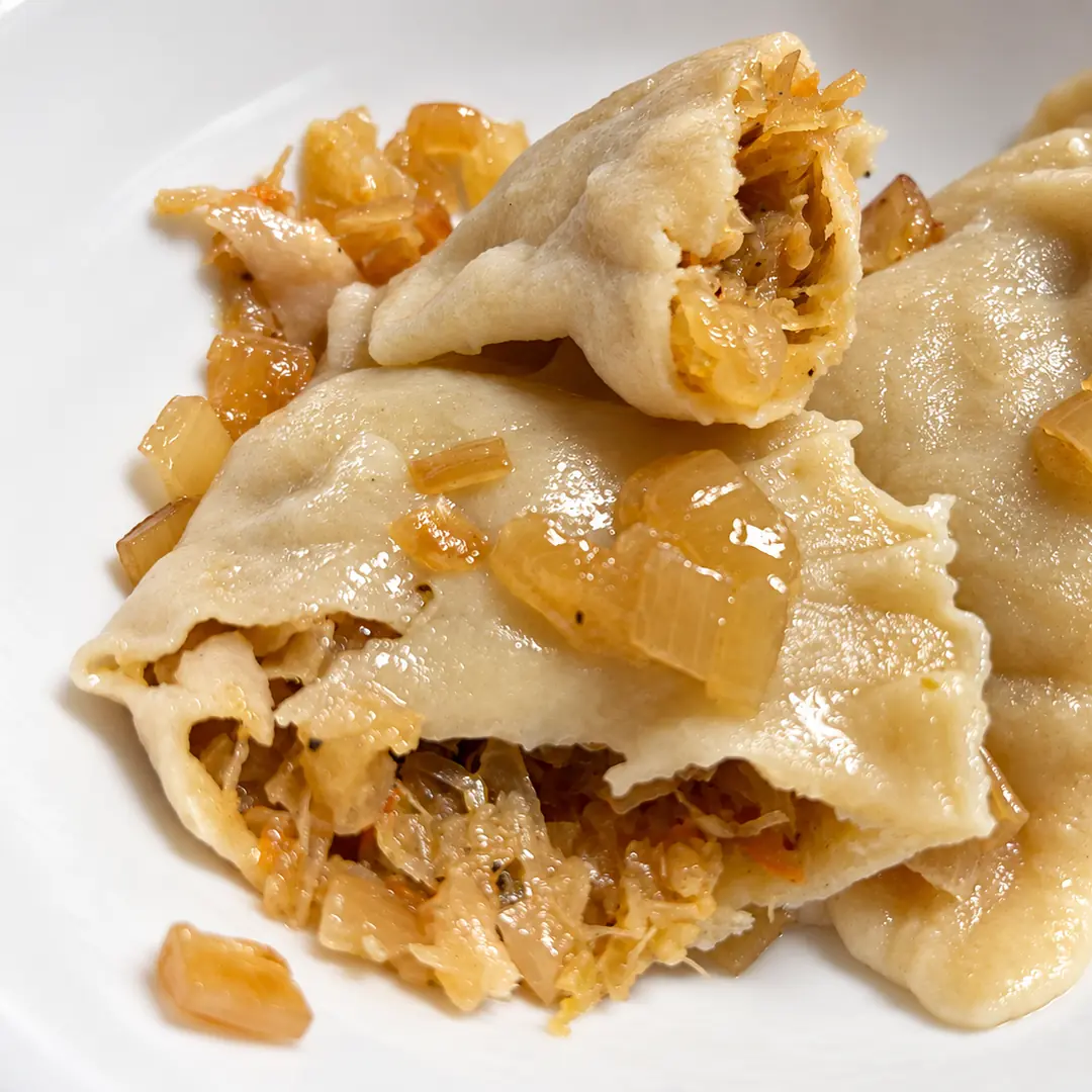 Handmade sauerkraut pierogies topped with buttery sautéed onions, with one cut open to show Kat’s house-made sauerkraut filling.