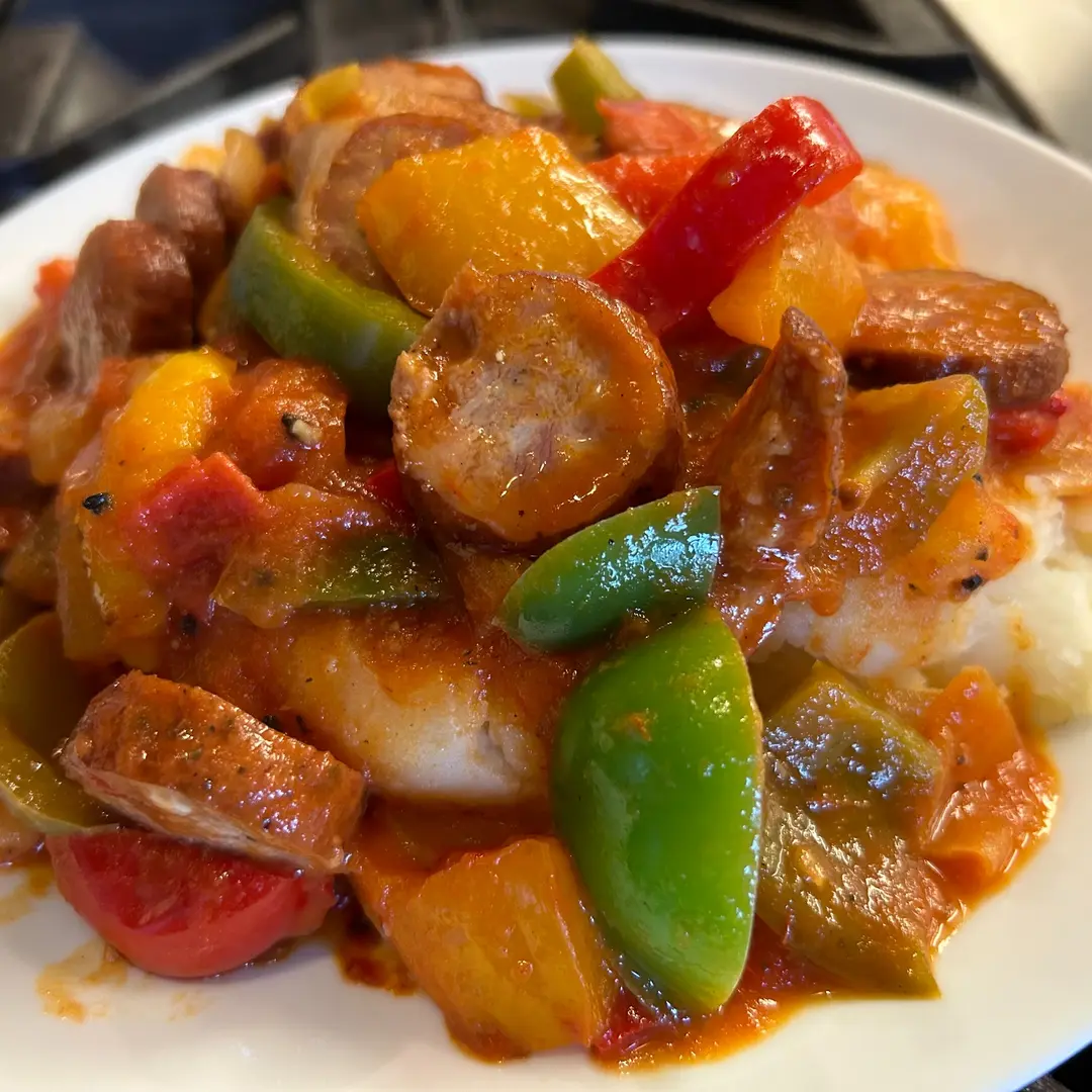 Sliced Polish kielbasa with vibrant red, green, orange, and yellow bell peppers and onions in Kat’s homemade tomato-based letcho sauce, served over mashed potatoes at Kat’s Café & Restaurant.