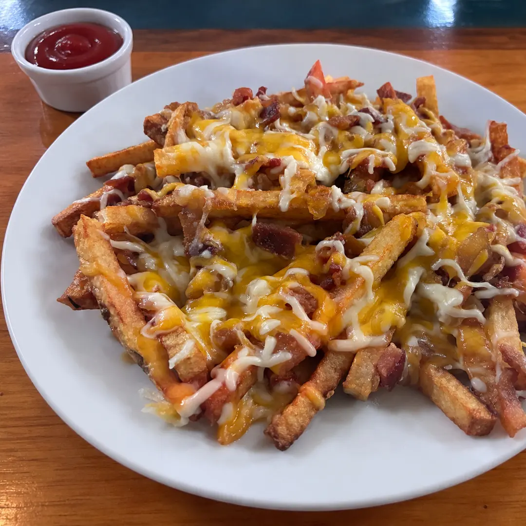 Fresh-cut loaded fries at Kat’s Café & Restaurant topped with melted cheese, crumbled bacon, and sautéed onions, served on a white plate with ketchup.