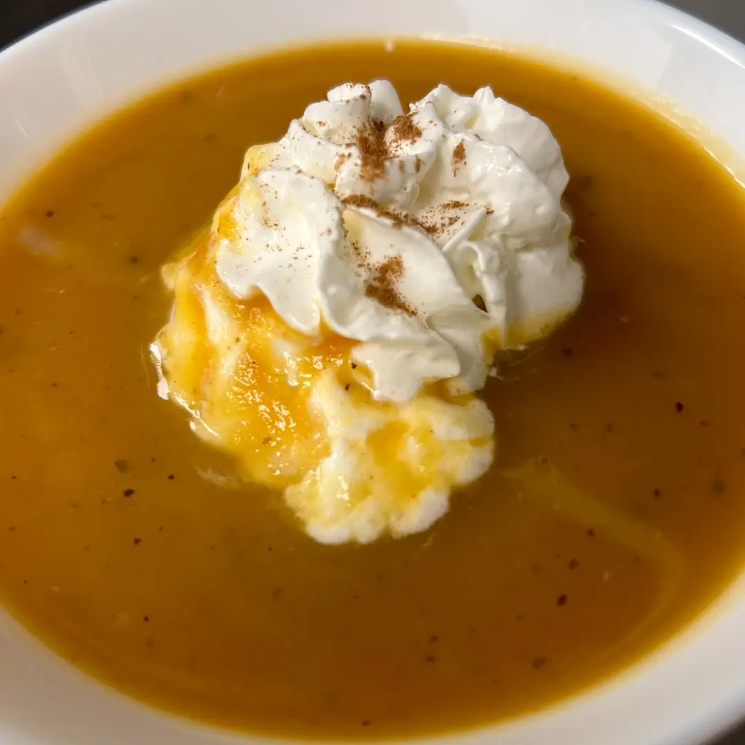 Creamy maple pumpkin soup at Kat’s Café & Restaurant, topped with whipped cream and warm spice in a white bowl.