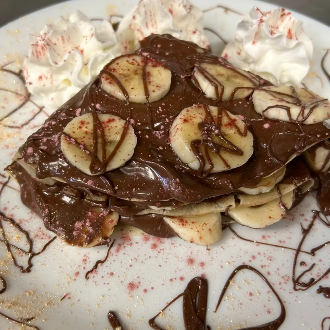 Freshly made crepe at Kat’s Café & Restaurant layered with Nutella and banana slices, topped with more Nutella, bananas, whipped cream, and chocolate drizzle.