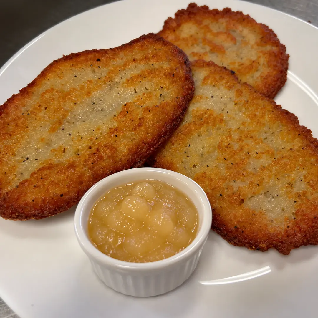 Three golden-brown potato bleenies at Kat’s Café & Restaurant served with a ramekin of applesauce.