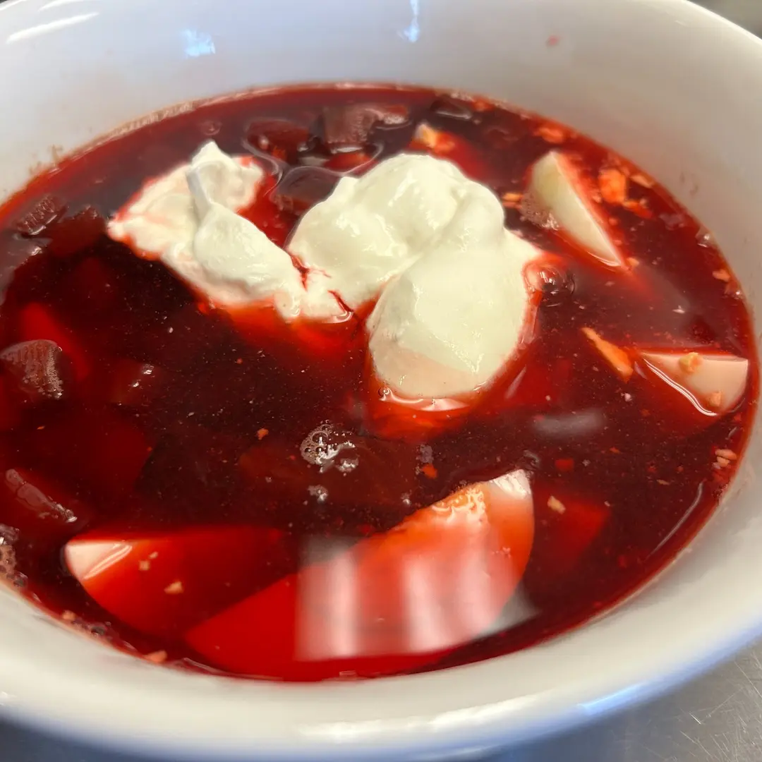Homemade red beet borscht at Kat’s Café & Restaurant, with beet pieces, hardboiled egg, and sour cream in a white bowl.