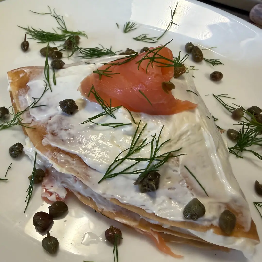 Folded crepe layered with cream cheese and smoked salmon lox, topped with capers and fresh dill on a white plate at Kat’s Café & Restaurant.