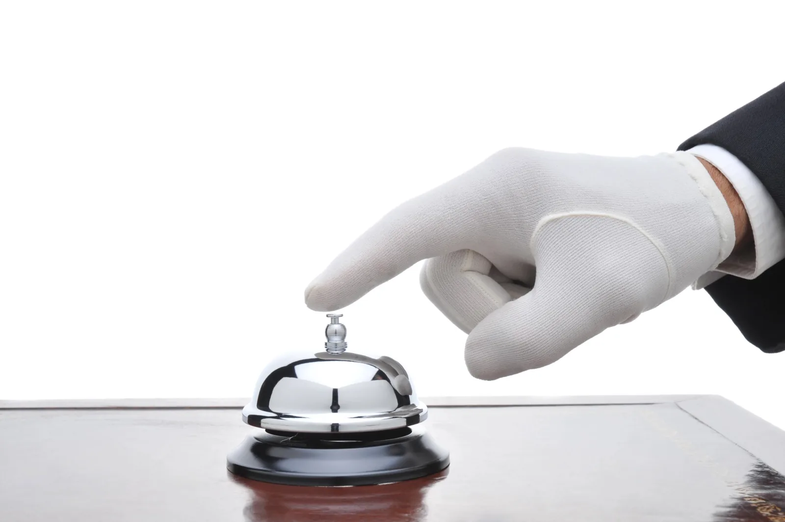 White-gloved hand poised above a silver service bell on a polished wooden table.
