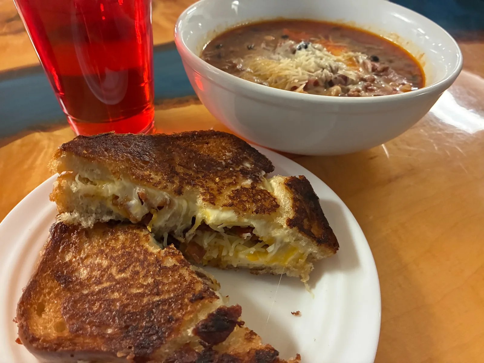 Toasted grilled cheese sandwich at Kat’s Café & Restaurant beside a glass of strawberry iced tea and a bowl of chili soup topped with shredded cheese on a wooden table.